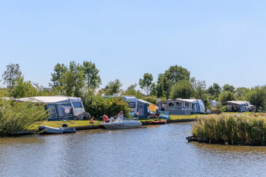Caravans op kampeerplaatsen direct aan het water met boten aangemeerd op Vakantiepark De Kuilart.