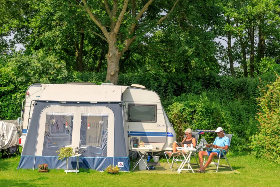 Ruime kampeerplaats met caravan en voortent op camping Ginsterveld in Zeeland